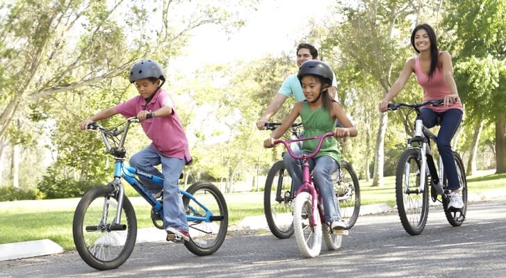 A mother and father riding bikes in the park with their little son and daughter